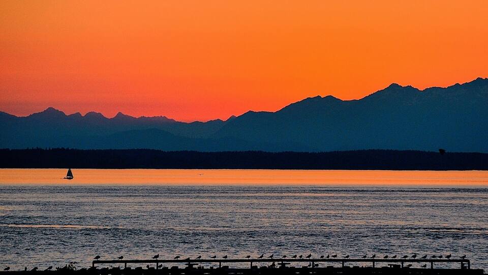 A sunset over a calm lake with mountains in the background and a pier with birds.