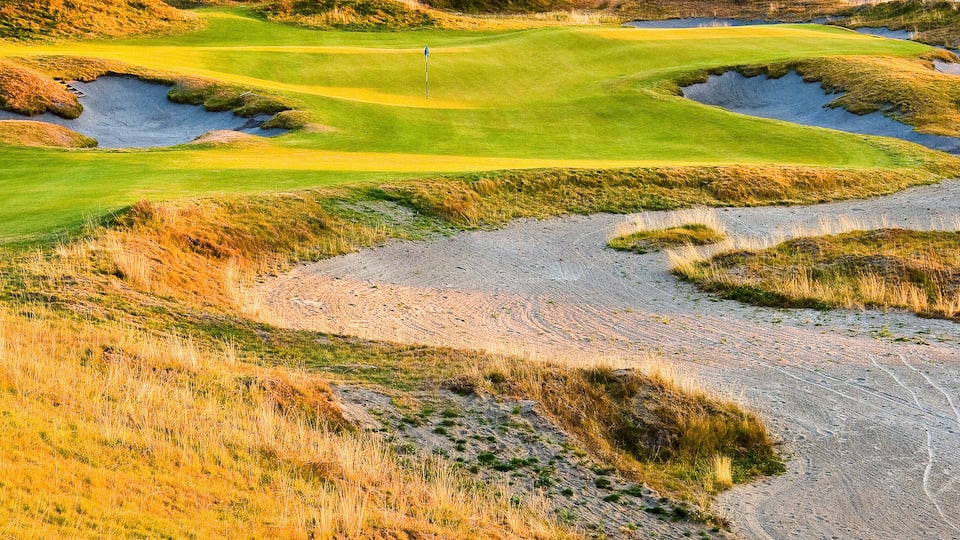 A golf course with sand bunkers and a flag on the green.