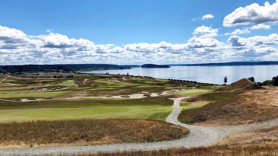 A golf course with a lake, a dock, and distant hills.