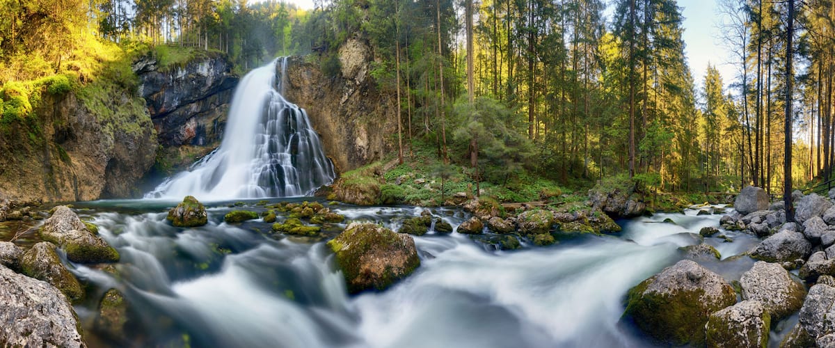 A waterfall cascading over rocks into a forested valley.