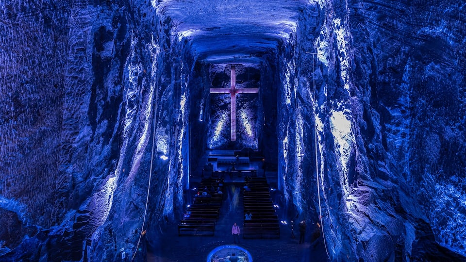 A cave with a cross at the end of a tunnel, benches, and a circular opening at the bottom.