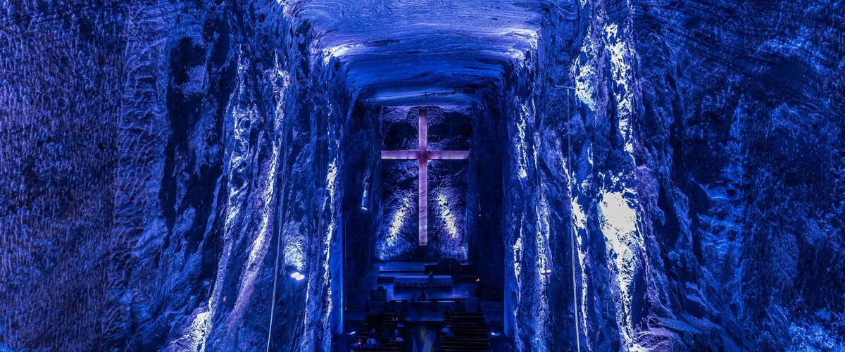 A cave with a cross at the end of a tunnel, benches, and a circular opening at the bottom.