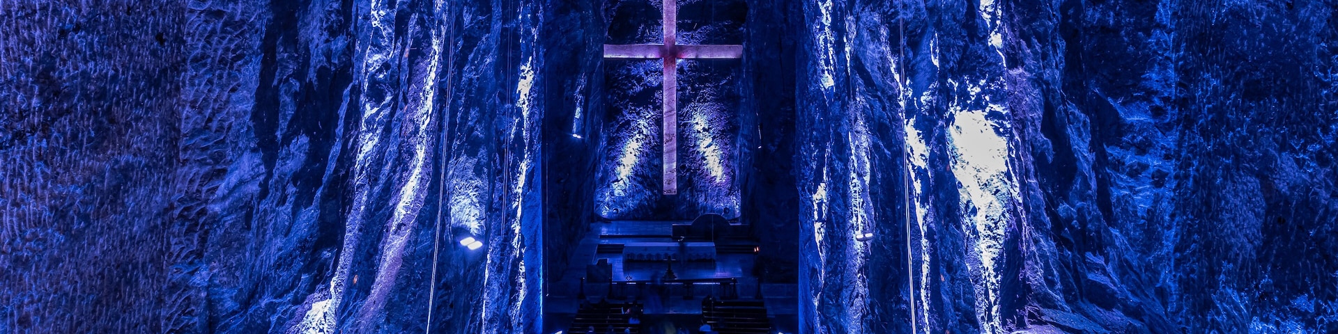 A cave with a cross at the end of a tunnel, benches, and a circular opening at the bottom.