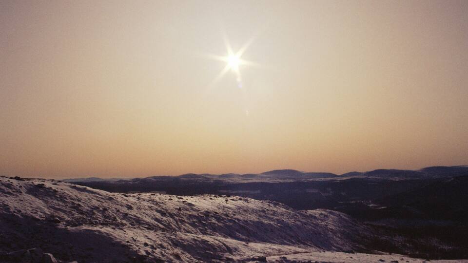 A snowy landscape with a bright star-like sun in the sky.