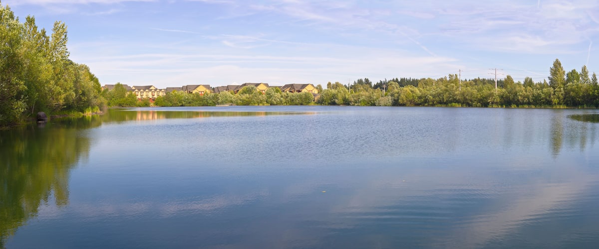 A calm lake with a reflection of trees and buildings.