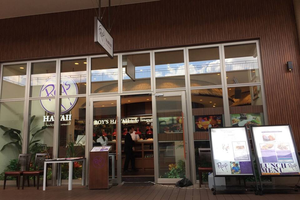 A restaurant with a large glass facade, signage for 'Roy's Hawaii', and a visible menu board outside.