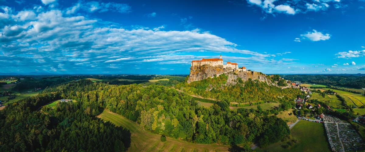 A castle on a hill with surrounding greenery and fields.