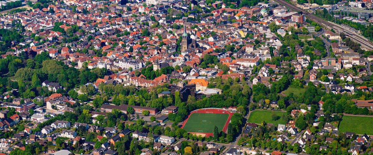 An aerial view of a densely populated town with a mix of residential and commercial buildings, a prominent church, and a large sports field.