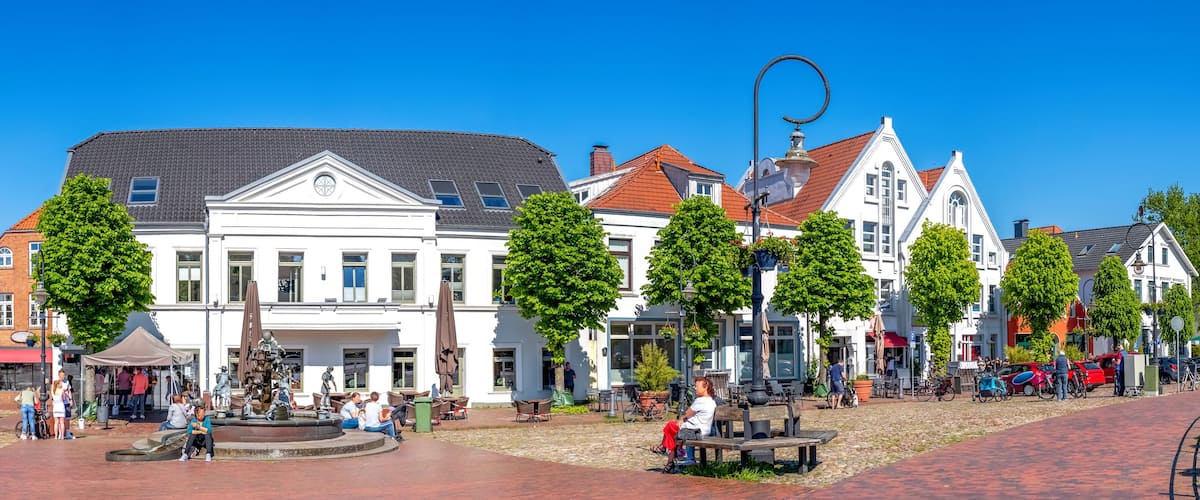 A cobblestone square with historic buildings, a fountain, and people sitting on benches.