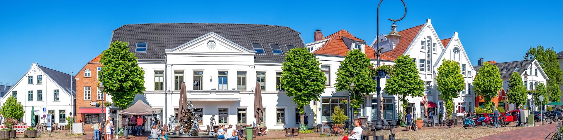 A cobblestone square with historic buildings, a fountain, and people sitting on benches.