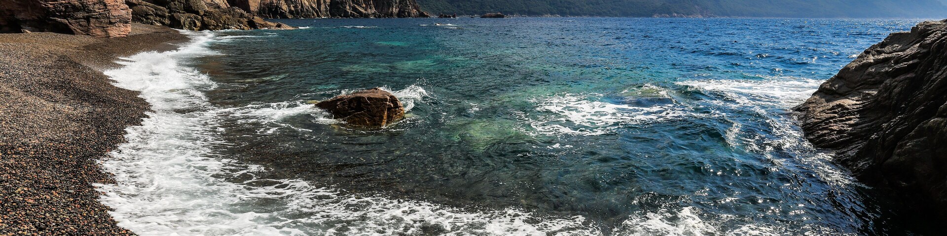 Una costa rocosa con aguas azules cristalinas y montañas al fondo.