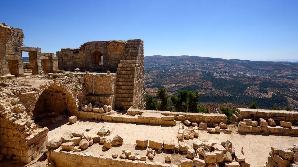 Ancient ruins with stone walls and arches, set against a backdrop of a mountainous landscape.