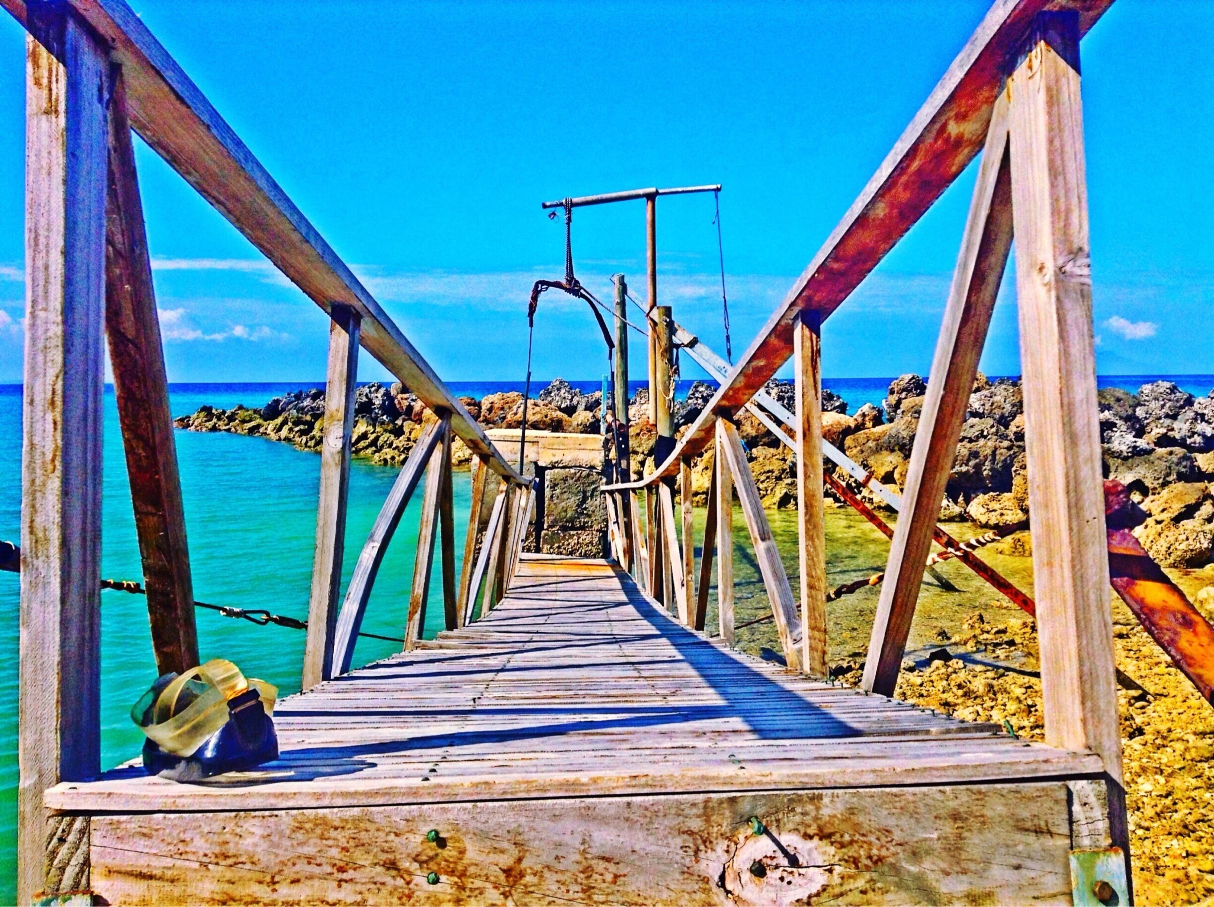 A wooden pier leading to a rocky shoreline with clear turquoise water.
