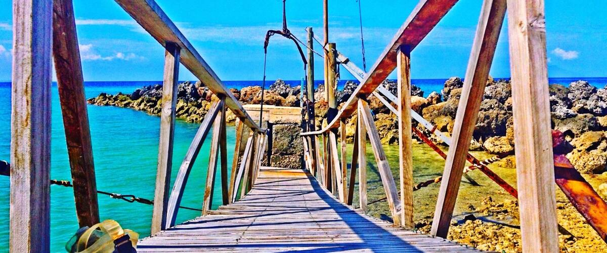 A wooden pier leading to a rocky shoreline with clear turquoise water.