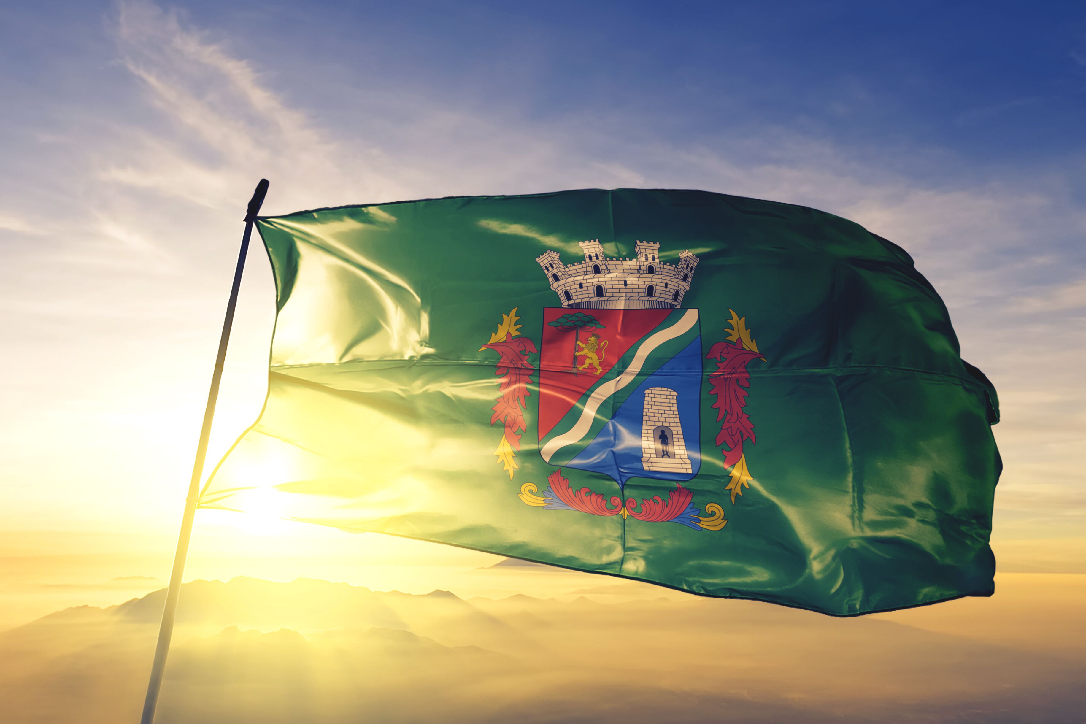 A flag with a castle emblem, waving in the wind against a sunrise.