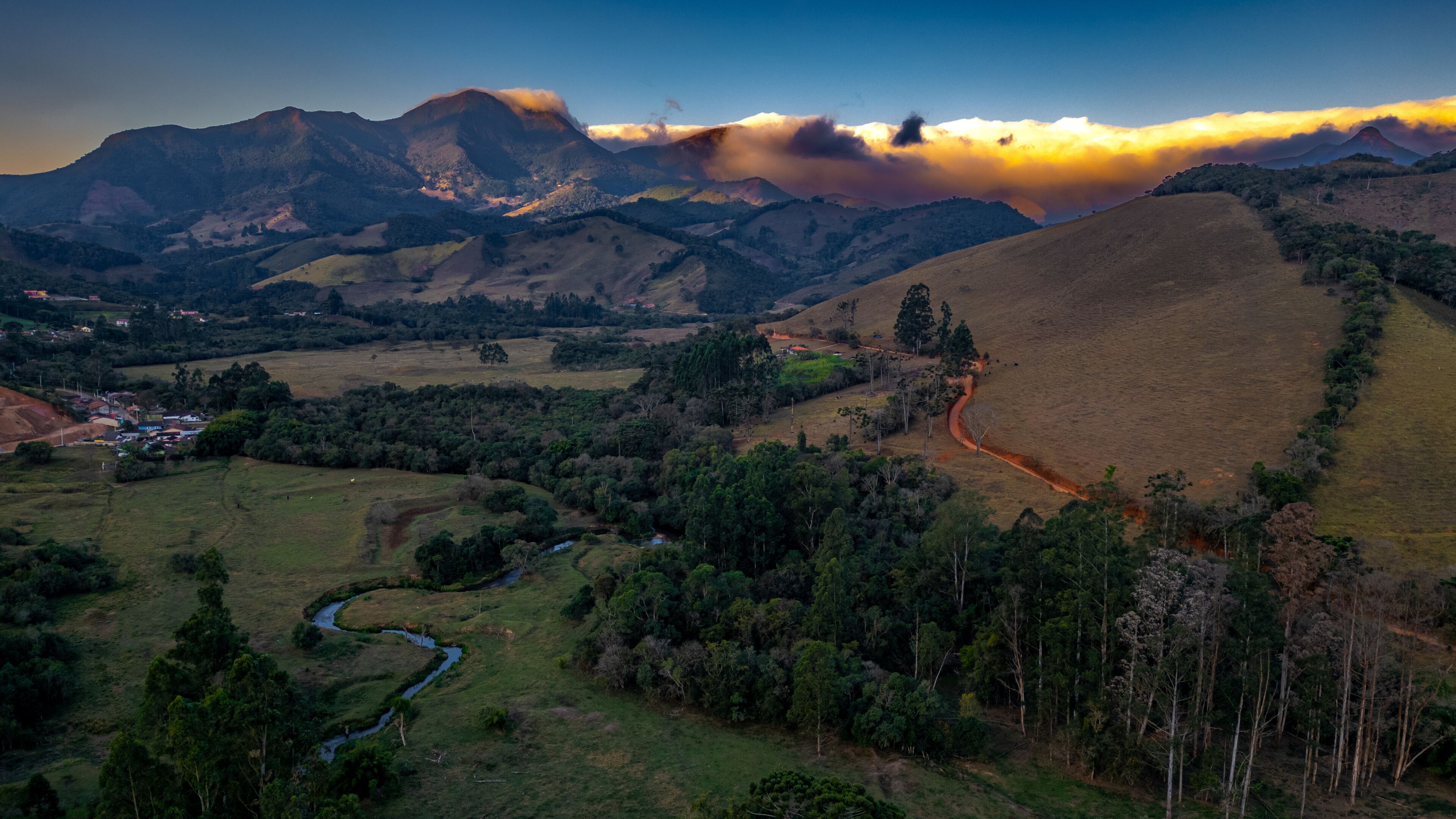 A mountainous landscape with a winding river, a small settlement, and a prominent mountain peak.