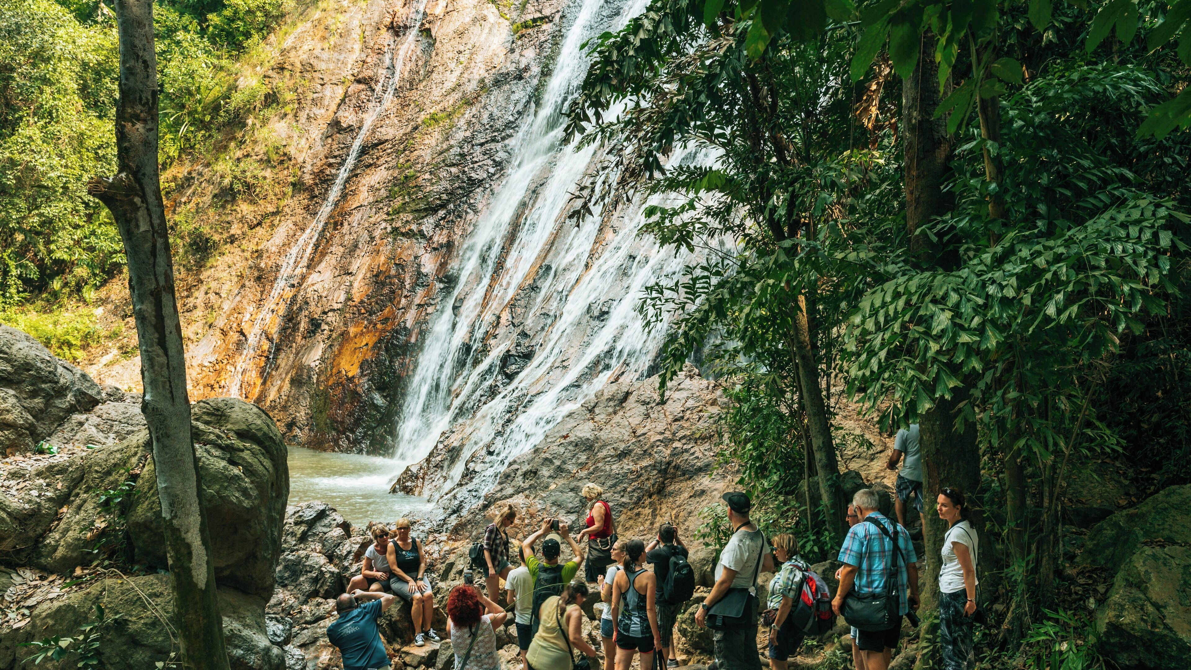 Visitors enjoying the natural beauty of Namuang Waterfall 1 in Koh Samui during a sunny day surrounded by lush greenery and rocky terrain