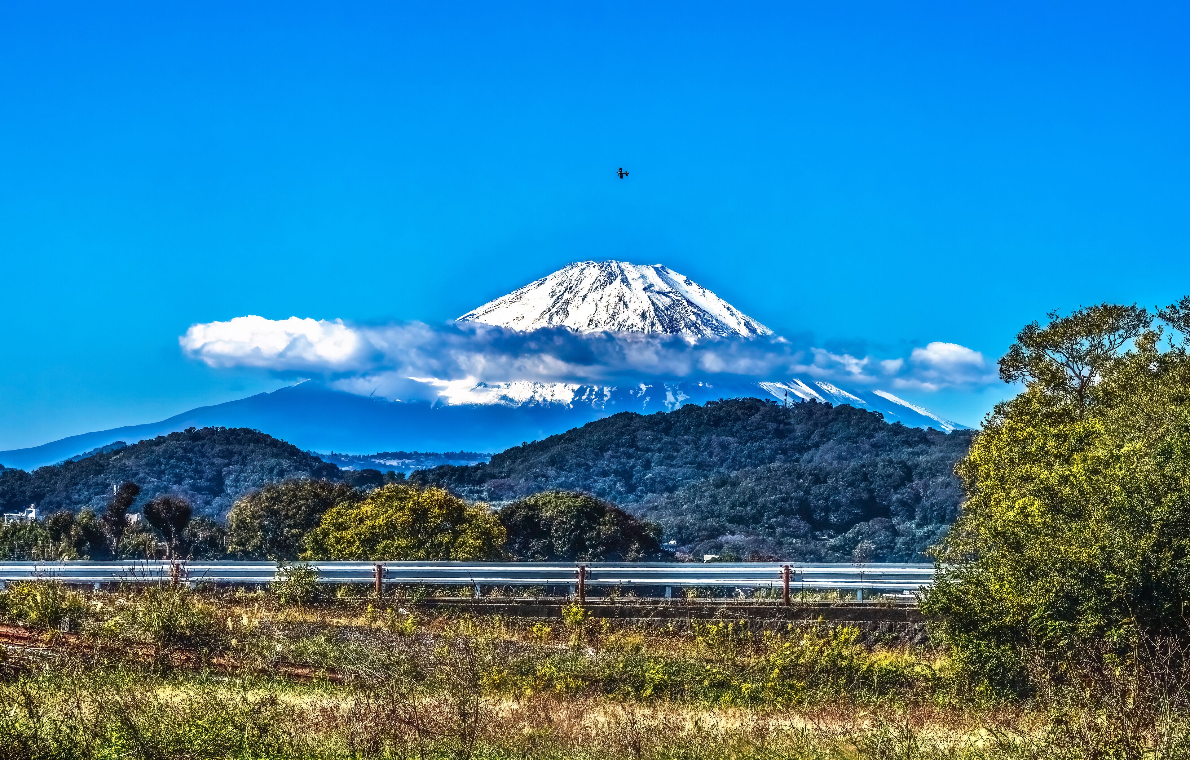 A snow-capped mountain, a clear blue sky, and a highway in the foreground.