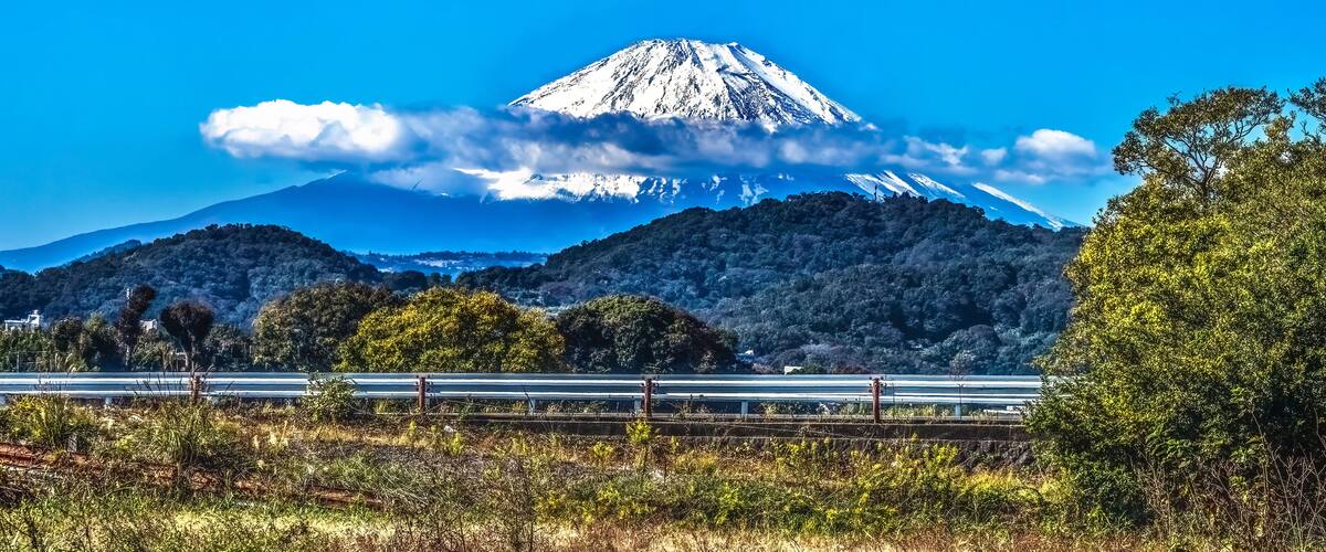 A snow-capped mountain, a clear blue sky, and a highway in the foreground.