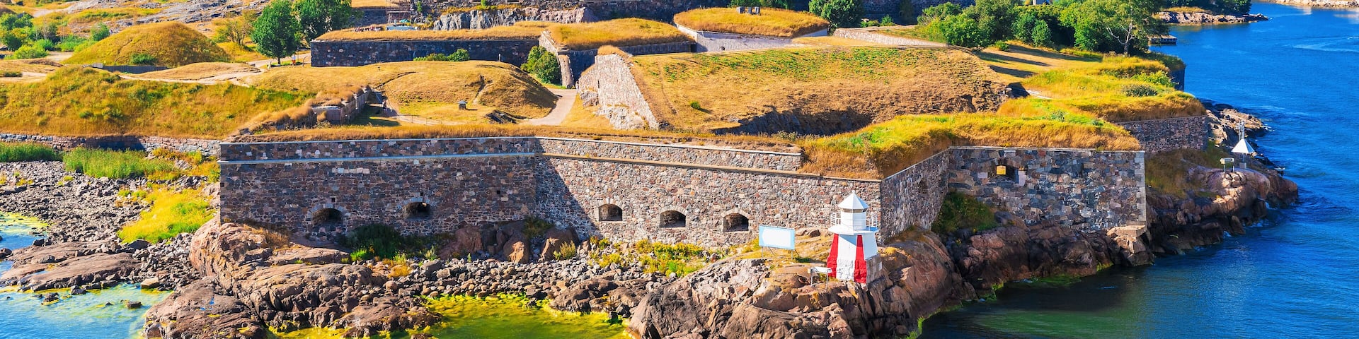 A coastal fortification with a lighthouse, surrounded by water and greenery.