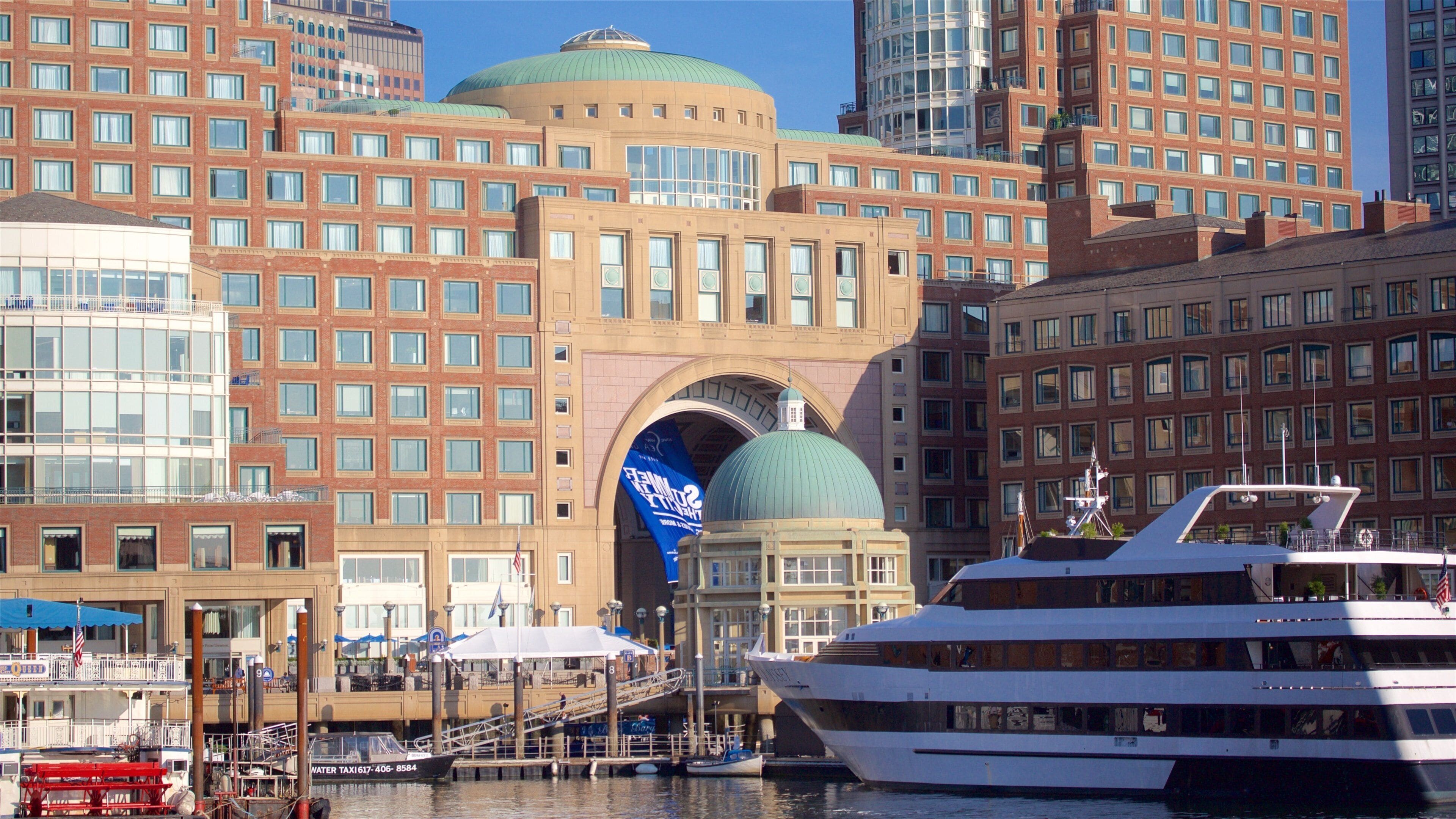 Un muelle con un gran crucero blanco amarrado, un edificio con cúpula verde y un banderín azul.