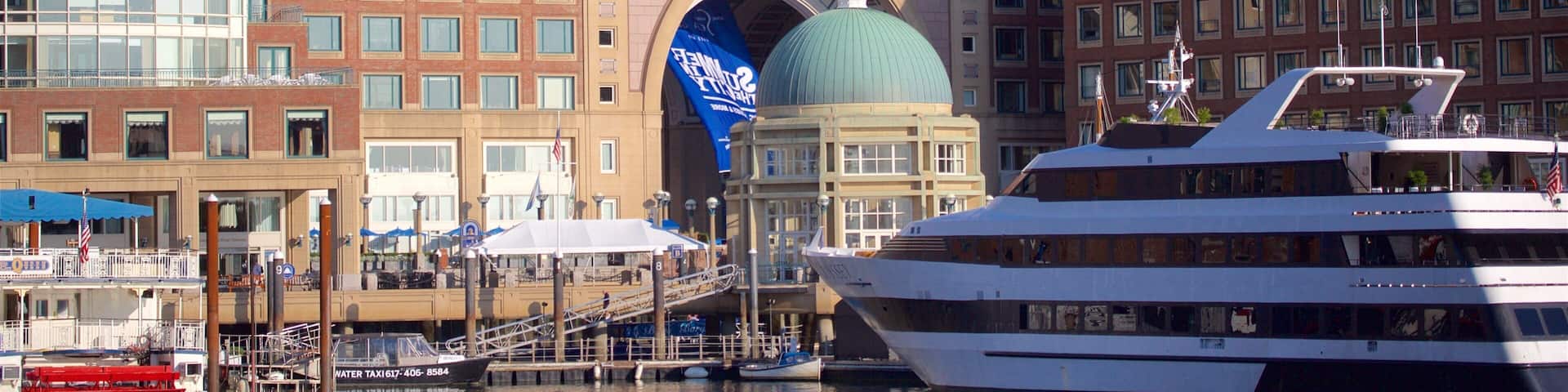 A waterfront with a large white cruise ship docked, a building with a green dome, and a blue banner.