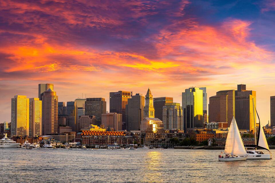 A city skyline at sunset with sailboats on the water.