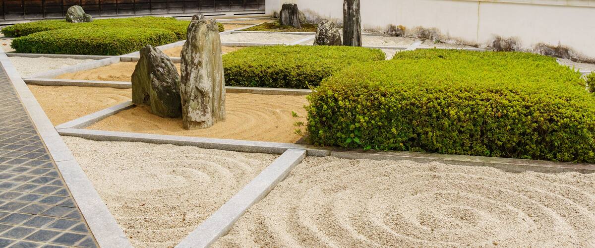 A traditional Japanese garden with neatly trimmed bushes, stone lanterns, and a tiled-roof building.