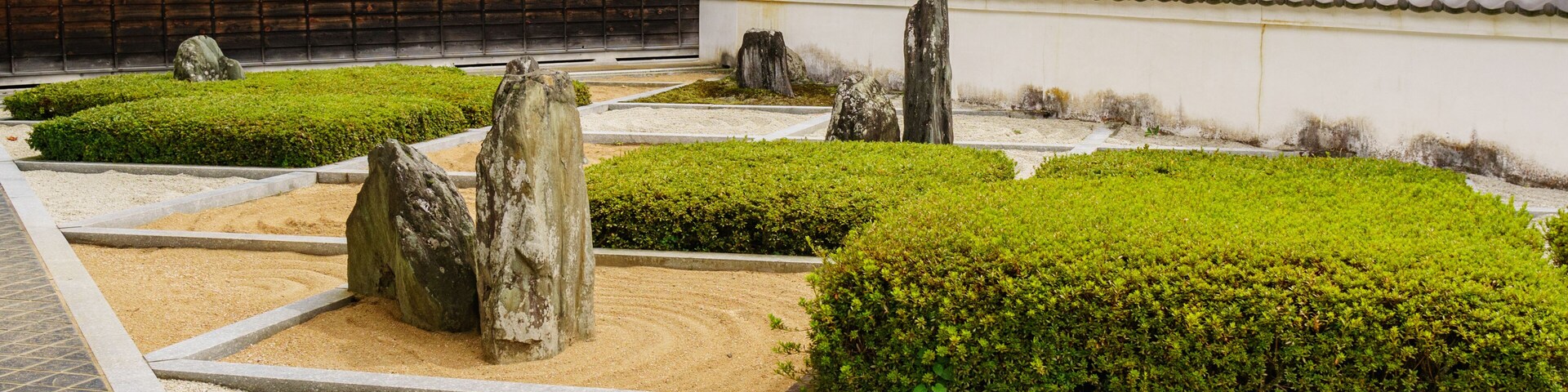 A traditional Japanese garden with neatly trimmed bushes, stone lanterns, and a tiled-roof building.