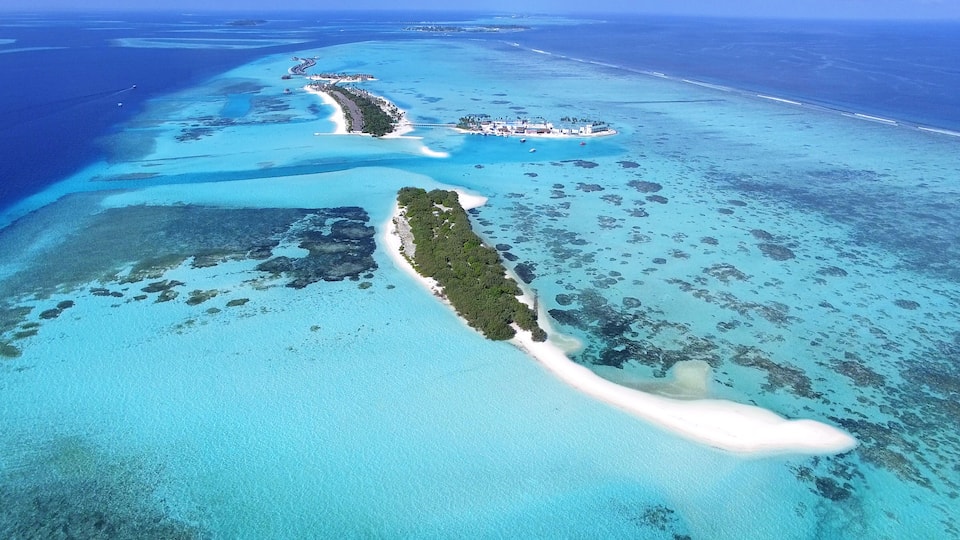 An aerial view of a tropical island with clear turquoise waters, a white sandy beach, and a small resort area.