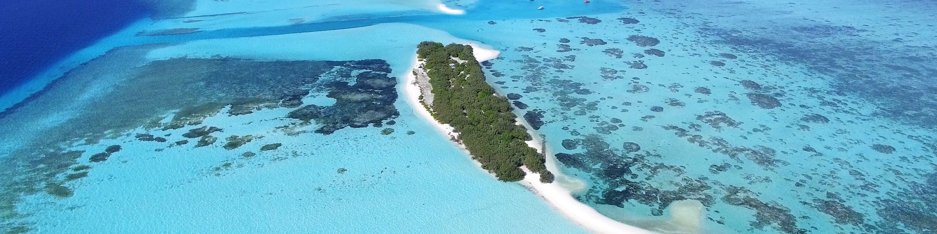Vista aérea de una isla tropical con aguas turquesas cristalinas, una playa de arena blanca y una pequeña zona de resort.