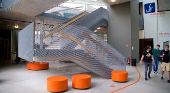 Een moderne kunstinstallatie met een metalen trap en oranje, cilindervormige stoelen.