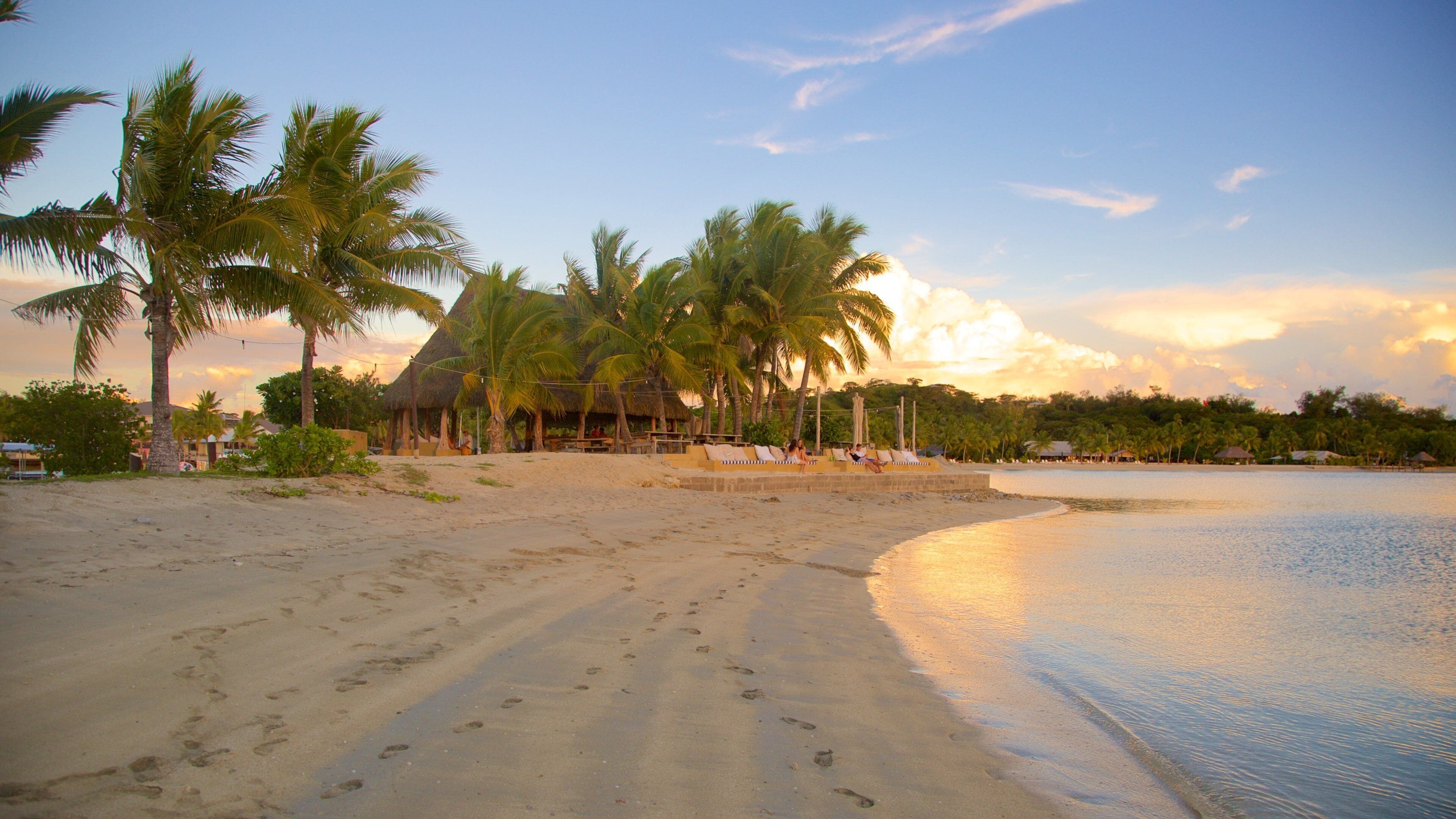 A beach with footprints, palm trees, and a thatched-roof structure.
