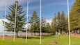 A park with tall white poles, green grass, and pine trees.