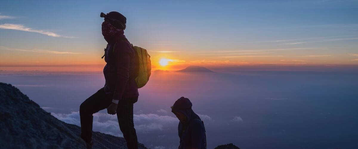 Two hikers on a mountain trail with a sunset in the background.
