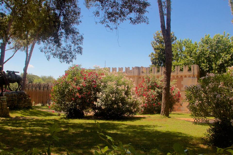 Jardí amb una estàtua, una muralla de castell i arbustos en flor.