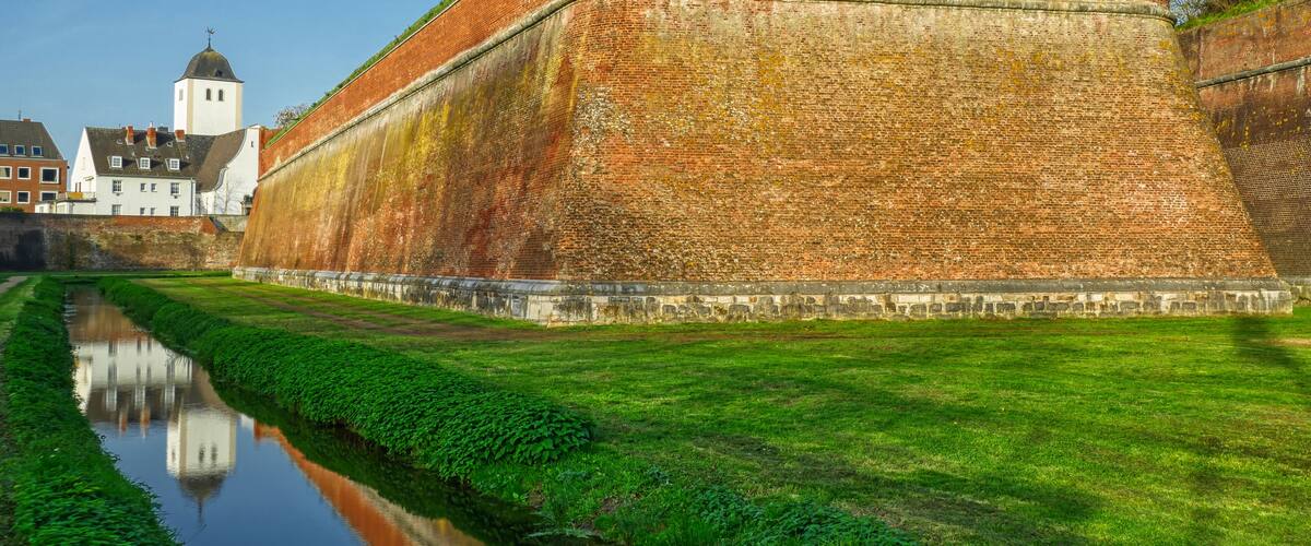 A large brick fort with a grassy embankment and a small canal in the foreground.
