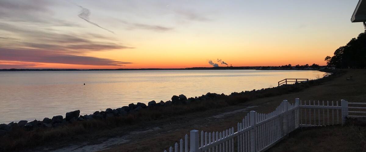 A sunset over a calm body of water with a white picket fence along the shore.