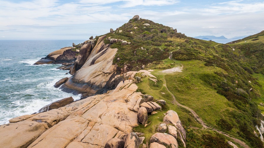 A coastal landscape with large boulders, a grassy hill, and the ocean.