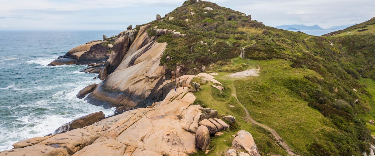 A coastal landscape with large boulders, a grassy hill, and the ocean.