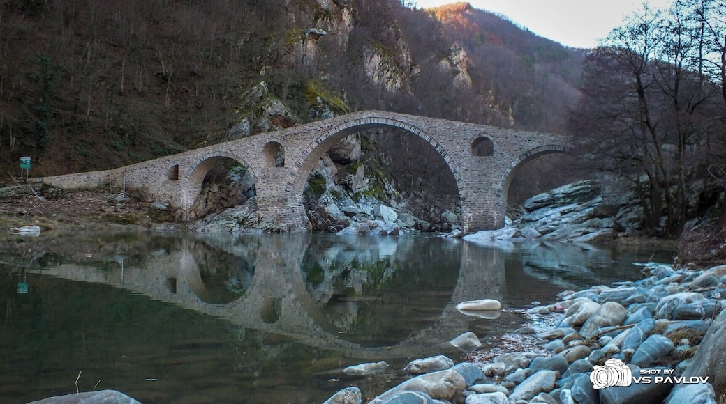 The Dyavolski Most (Devil’s Bridge), (also known as Sheytan Kyupriya) is a medieval bridge over the Arda river in Bulgaria. It is situated in a picturesque valley about 10 kilometers northwest of the town of Ardino and 4 kilometers east of the village of Galabovo (municipality of Banite).
The bridge was built in 1515 - 1518 by the builder Dimitar from the village of Nedelino (which is a town nowadays) upon the remains of an ancient Roman bridge on the road, linking the Aegean region with Northern Thracian valley (Gornotrakiyski Nizina) through the Makaza pass.
The bridge is situated 420 meters above sea level and is surrounded on both sides by steep slopes. Its length is 56 meters, and its width is 3.5. The bridge has three vaults; it has holes with small arches in its side vaults, made for drainage. The height of the middle vault is 11.5 - 12 meters, with a stone parapet on the edge, 12 cm high.
In 1984 the bridge was declared a cultural monument. The bridge can be reached by car, passing along a rough road. Tourist infrastructure had been built near it for picnic and recreation.
