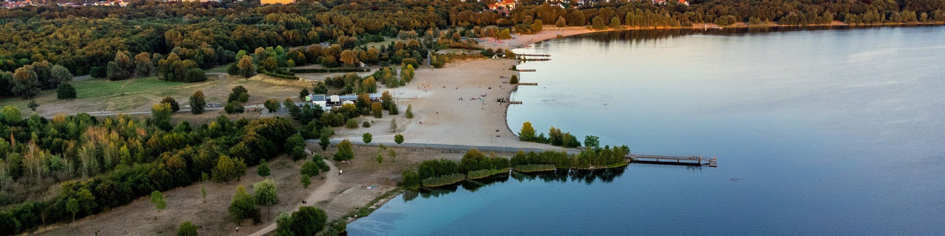 Un pueblo junto al lago, con playa, muelle y abundante vegetación.