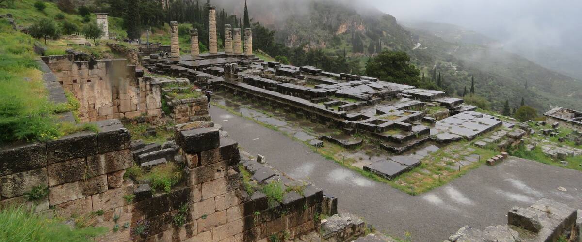 Ancient ruins with stone structures and columns, surrounded by misty mountains and greenery.