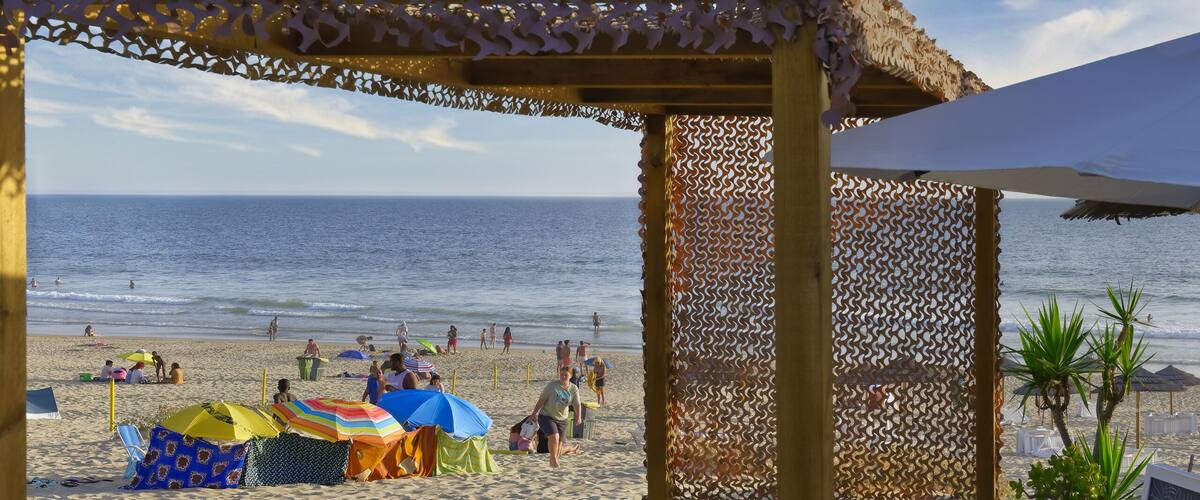 A beach with a wooden deck, umbrellas, and a beach hut.