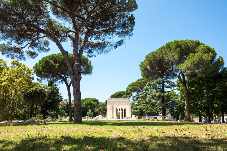 A historic building with columns, surrounded by large trees and a grassy field.