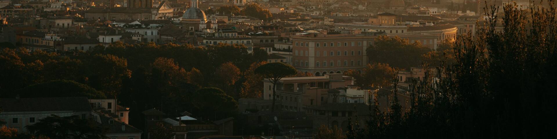 A cityscape at sunset with prominent historical architecture, including domed buildings and a central monument.