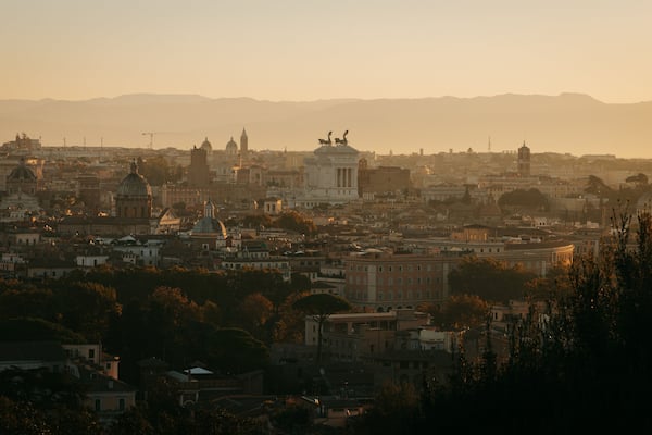 A cityscape at sunset with prominent historical architecture, including domed buildings and a central monument.