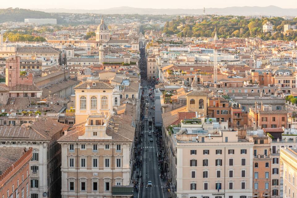 Vista panorámica de una ciudad densamente construida con arquitectura histórica, incluyendo cúpulas destacadas y una calle central flanqueada por edificios.