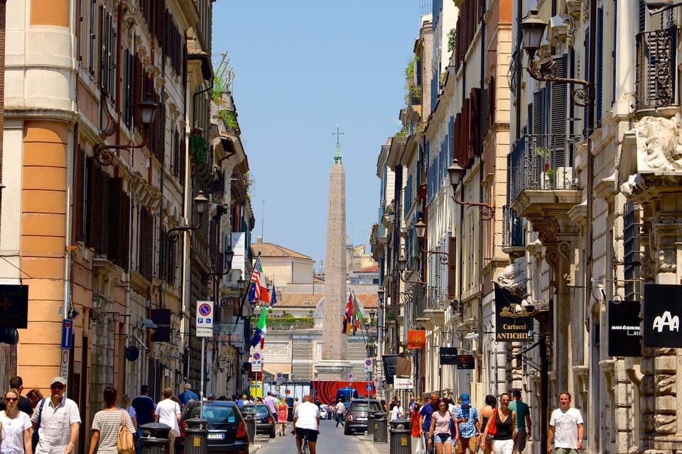 Una calle concurrida, edificios históricos, un obelisco alto y varias banderas.