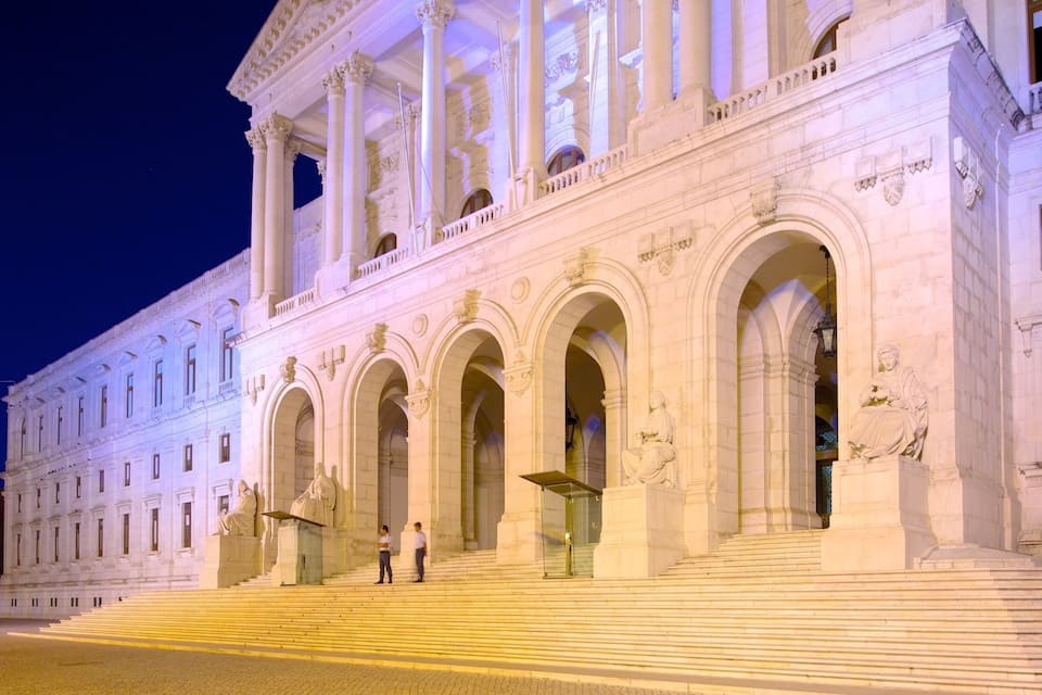 A grand neoclassical building with large columns and arched doorways, illuminated at night.